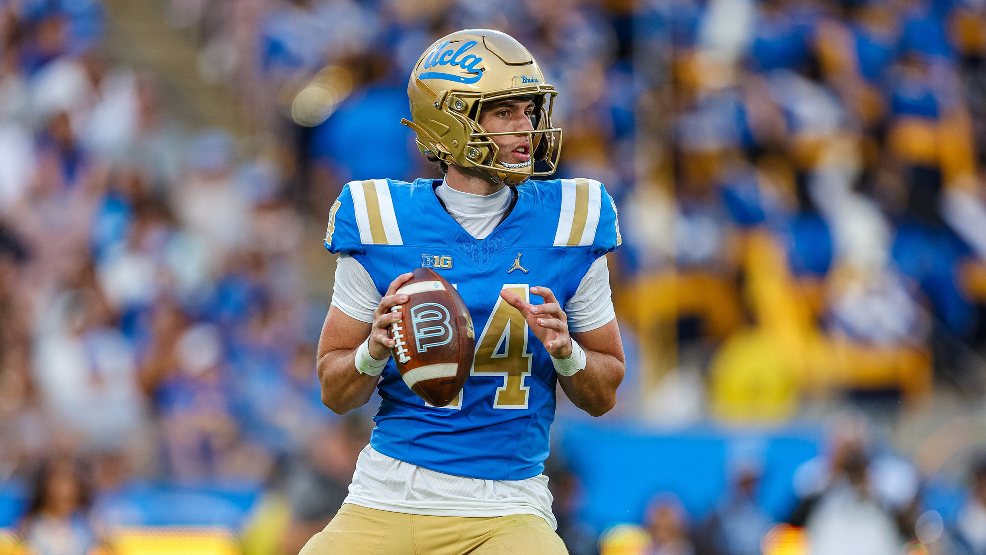 UCLA quarterback Ty Dieffenbach gets ready to throw a football during the Bruins' win over Wisconsin at the Rose Bowl. Dieffenbach holds the football in his right hand; fans fill the stands in the background, which is blurry from the focal length of the camera.