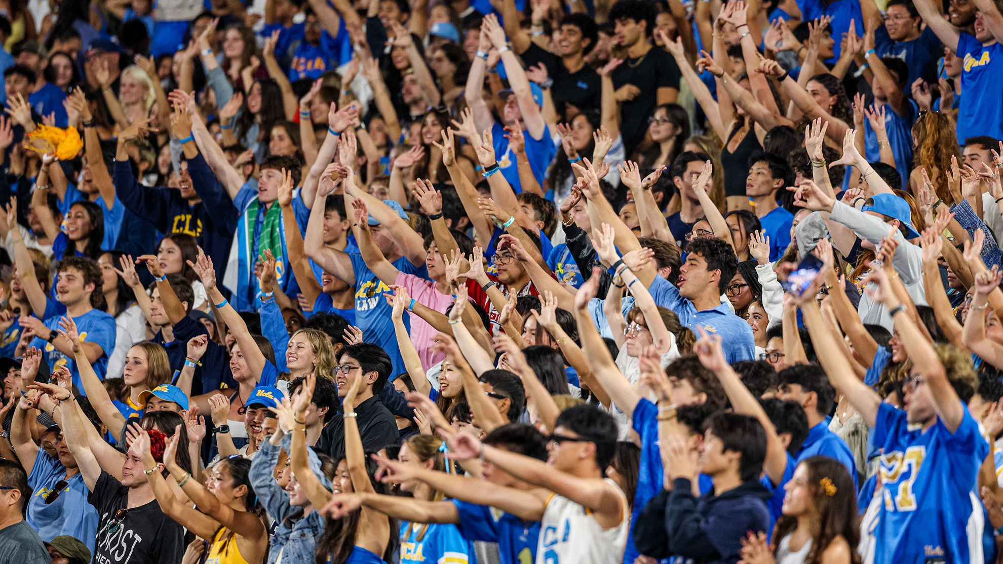 Fans hold their arms in the air during a UCLA football game at the Rose Bowl