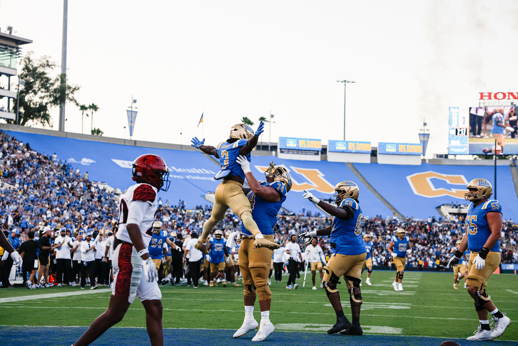 Wayne Knight celebrates in the endzone, jumping with his arms and legs in a star formation while an offensive lineman picks him up.