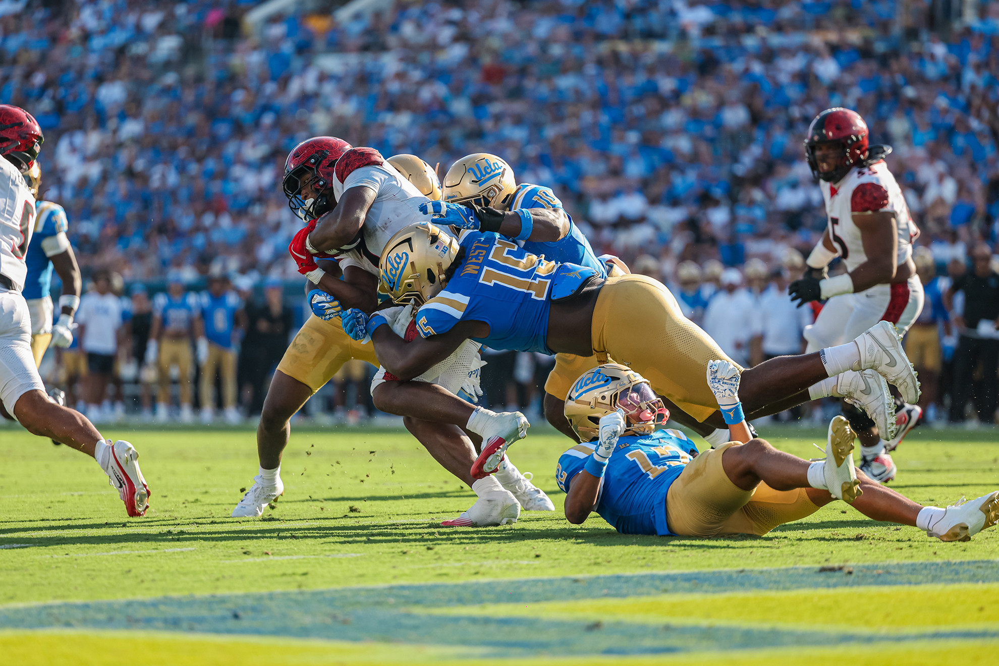 Three UCLA defensive players make a tackle on an SDSU running back.