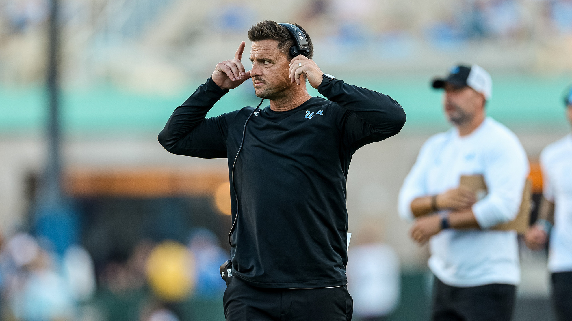 Bob Chesney adjusts his headset and looks out onto the field during a game